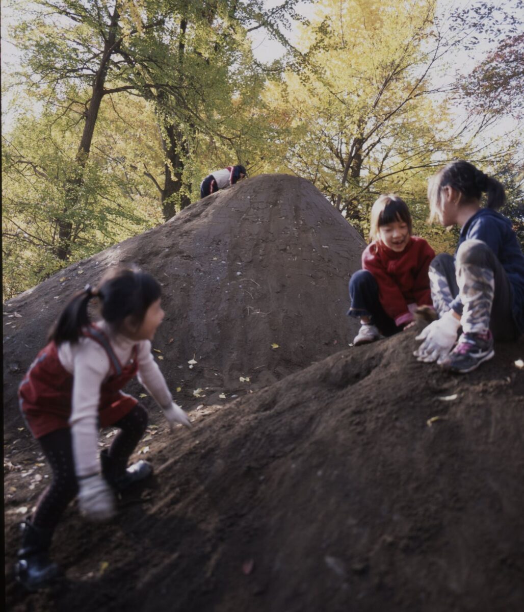 森の中に盛られた２つの土の山に、子供たちがよじのぼって遊んでいる