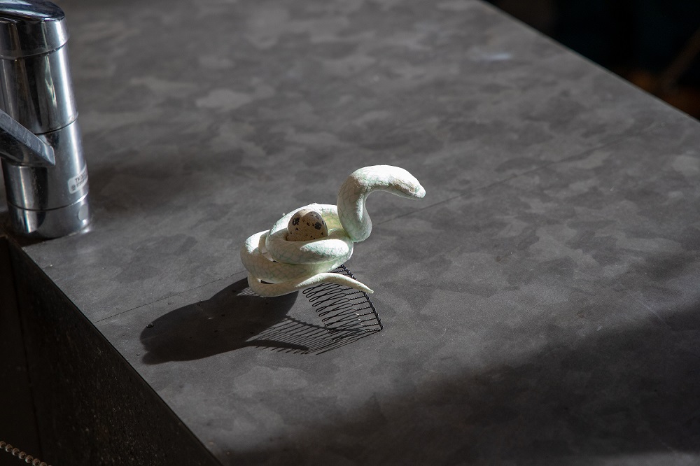 トグロを巻いた白い蛇が象られた髪飾りが水道の横に置かれている風景