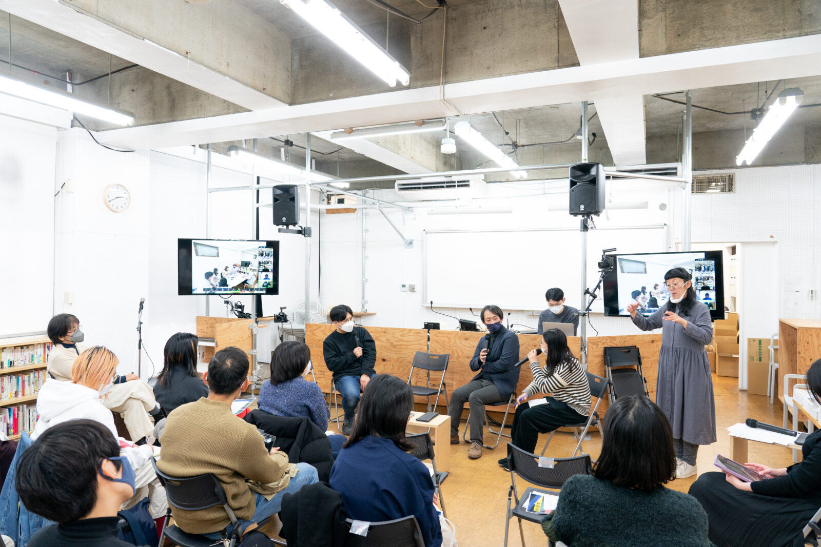 3人が椅子に座って話していて、その横で手話通訳をしている人がいる様子を10人ほどが見ている