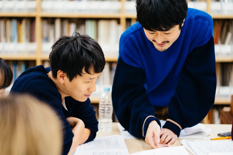 机の上の資料をのぞき込む、萩原さんと井山さん