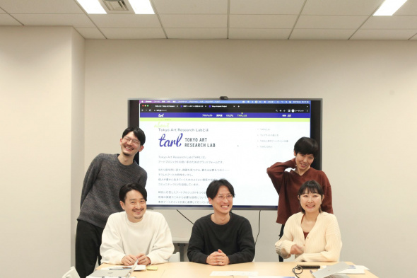 TARLウェブサイトが映った大型モニターの前に並ぶプロジェクトメンバー。手前左側から萩原さん、井山さん、川村さんが座り、その後ろに左から櫻井さんと小山さんが並んでいる