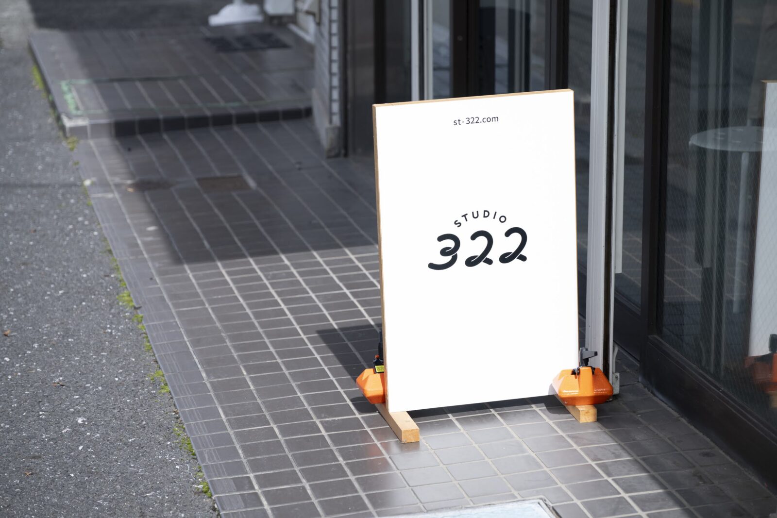 道路に立っている、膝の高さほどの白い看板にSTUDIO322のロゴマークが描かれている